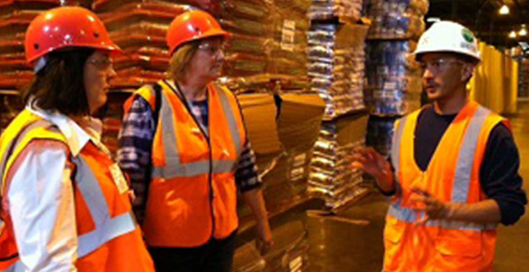 Associates standing in front of pallets of dog food with hard hats on