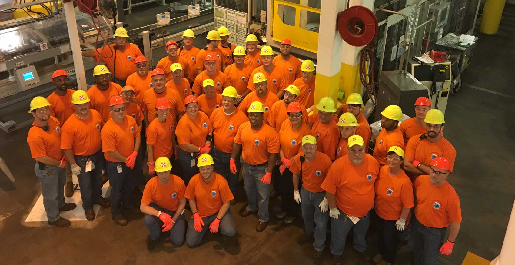 Group of people standing on factory floor with hard hats on