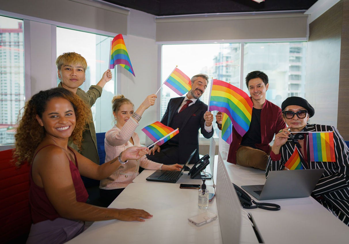 Group of employees waving Pride flags in conference room