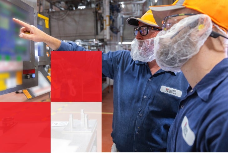 Two men in a factory looking at a screen displaying a red square, engaged in discussion about their work