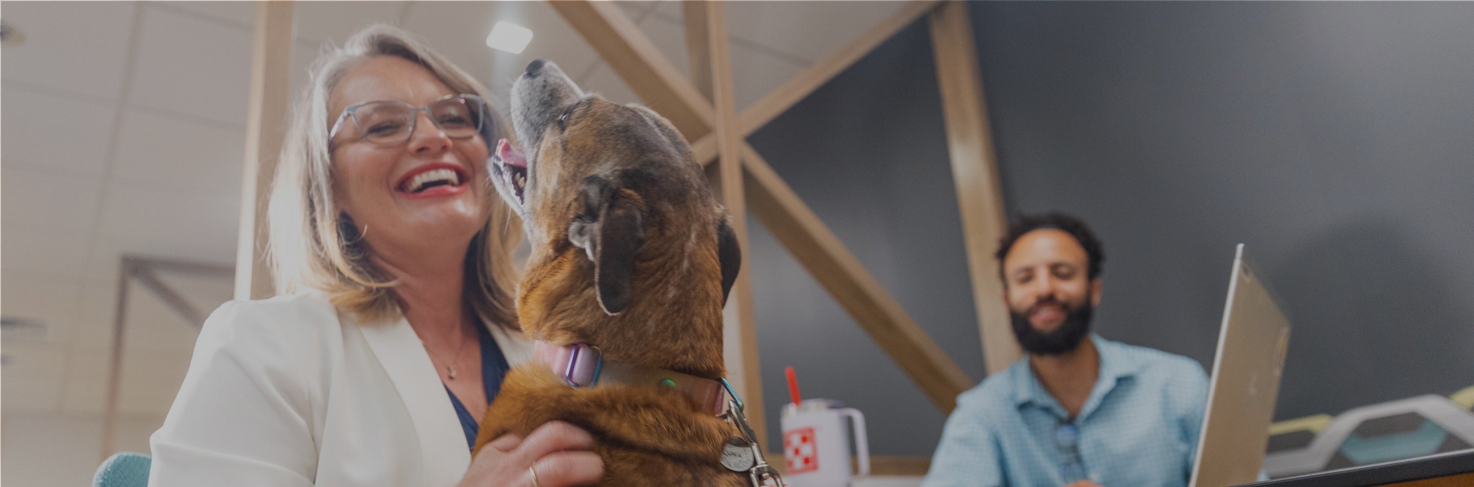 A woman sits at a desk with her dog, both looking relaxed and content in their shared workspace.