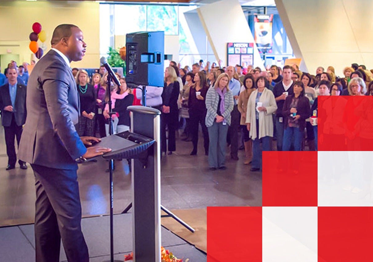 A man in a suit delivers a speech to an engaged audience, showcasing confidence and leadership