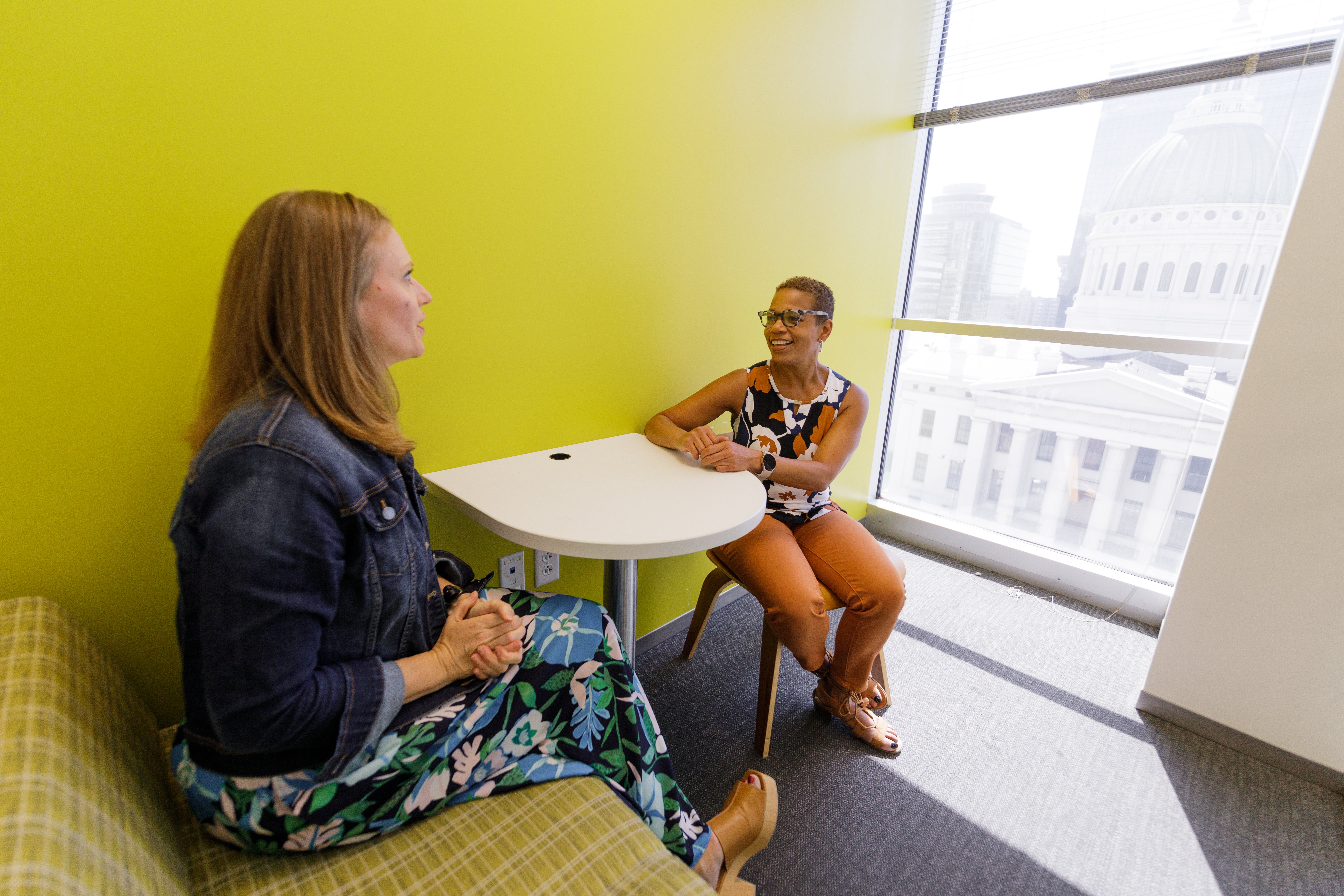 Two women engaged in conversation sit at a small table in a bright room