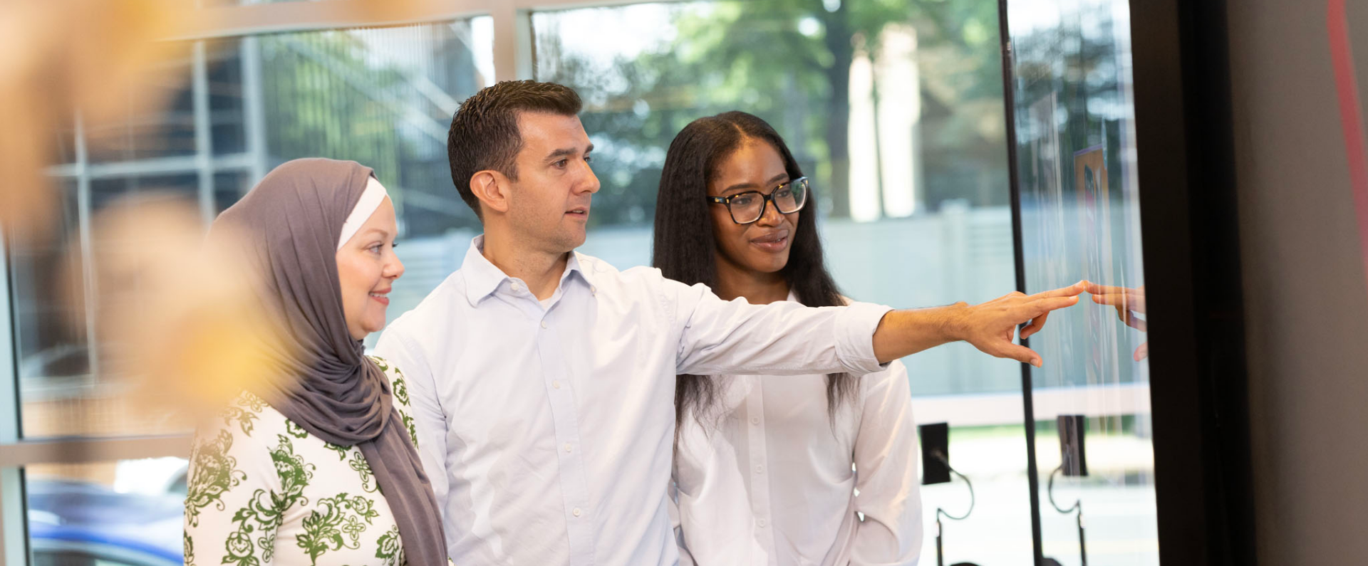 Three people standing, engaging with a large monitor on the wall